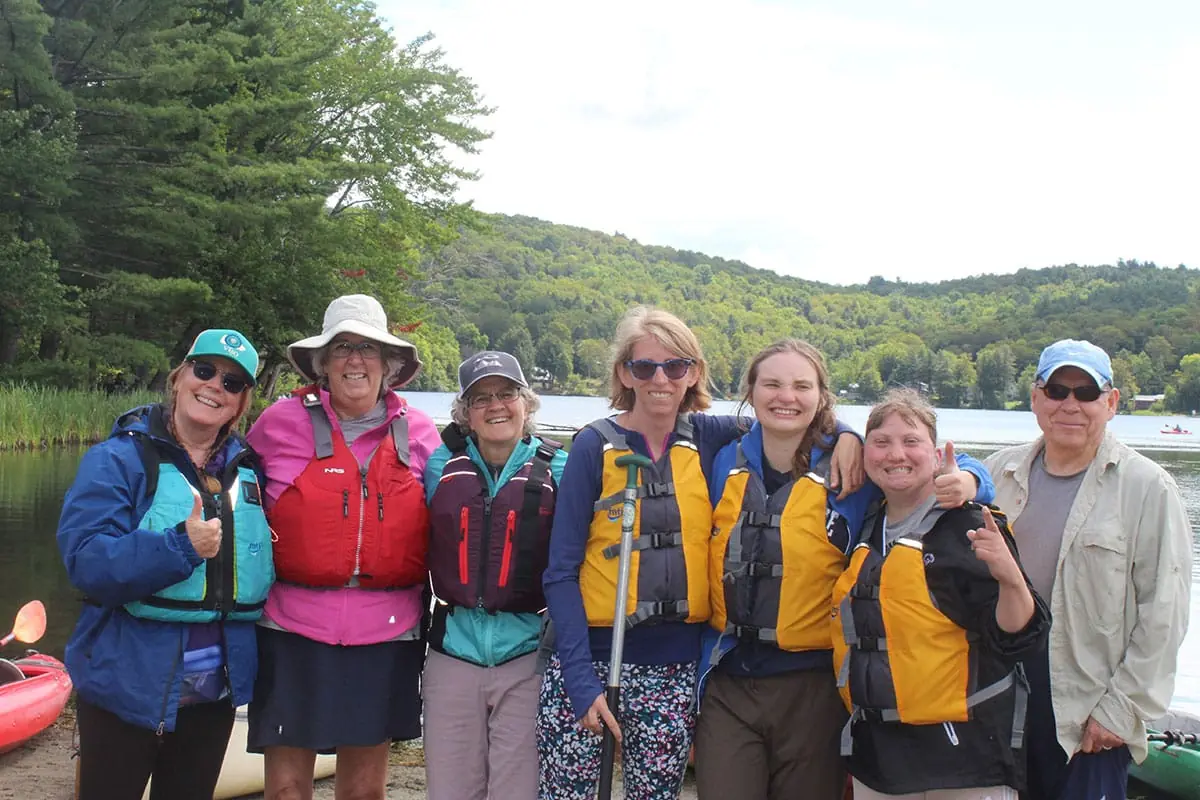 A group in life jackets on the shore of a lake before a paddling trip