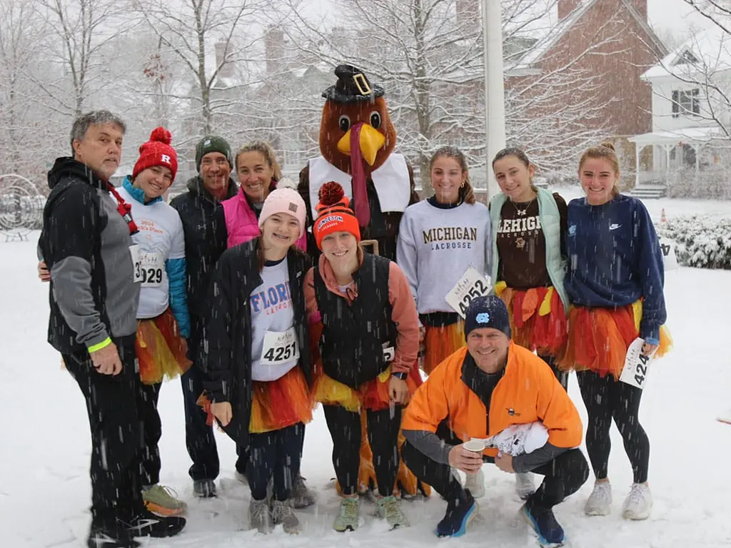 Turkey Trot volunteers in tutus posing in the snow with the turkey mascot