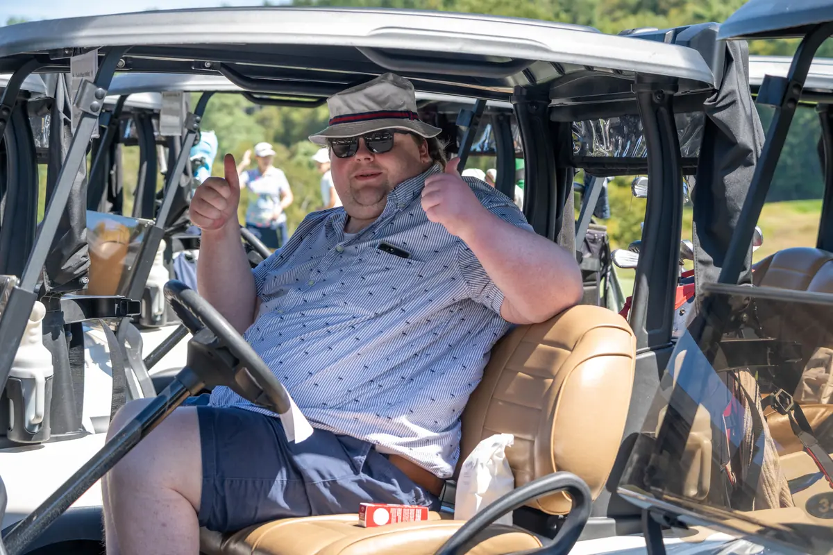 A participant giving two thumbs up from the seat of a golf cart