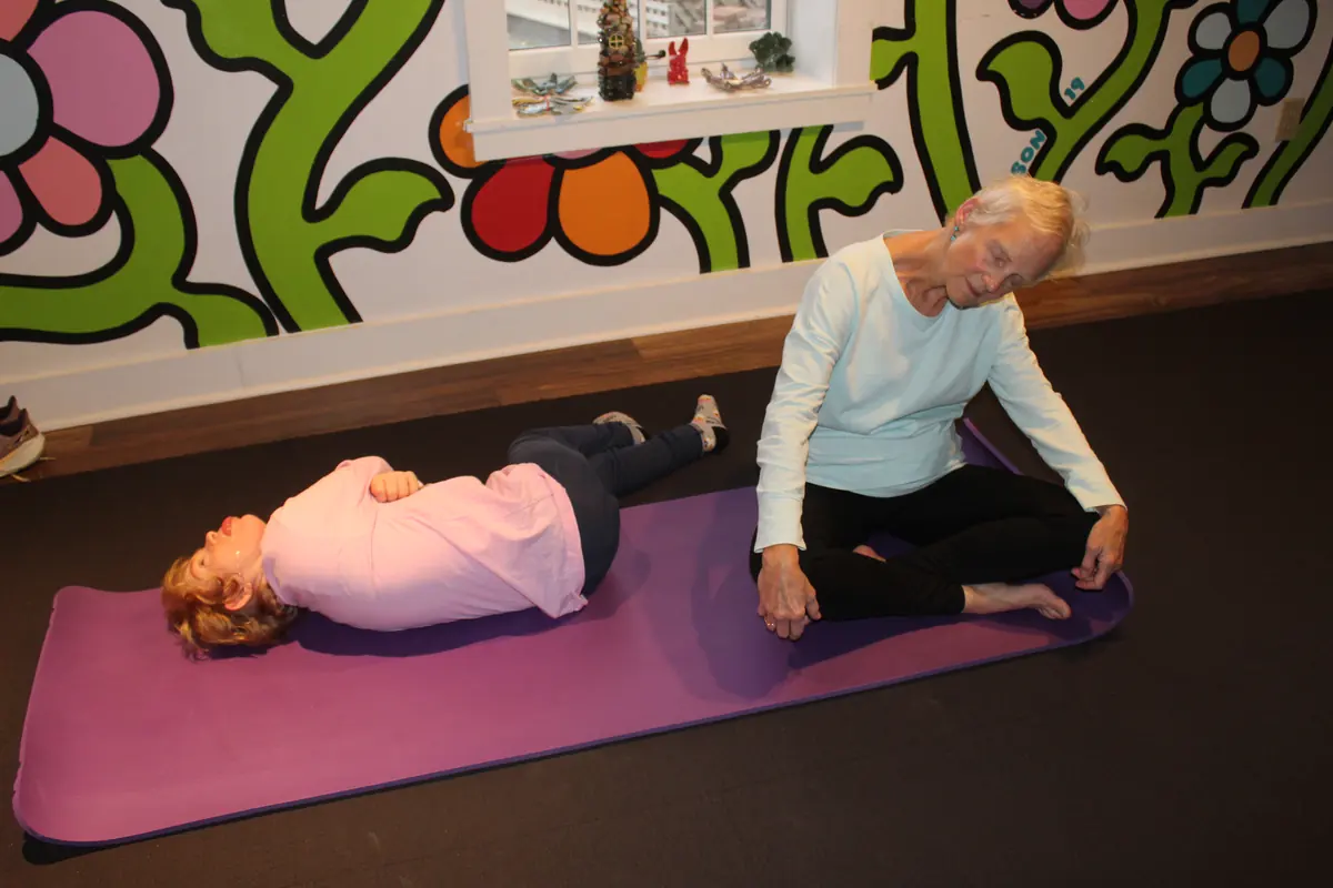 A yoga instructor leading a participant through a stretch on a mat