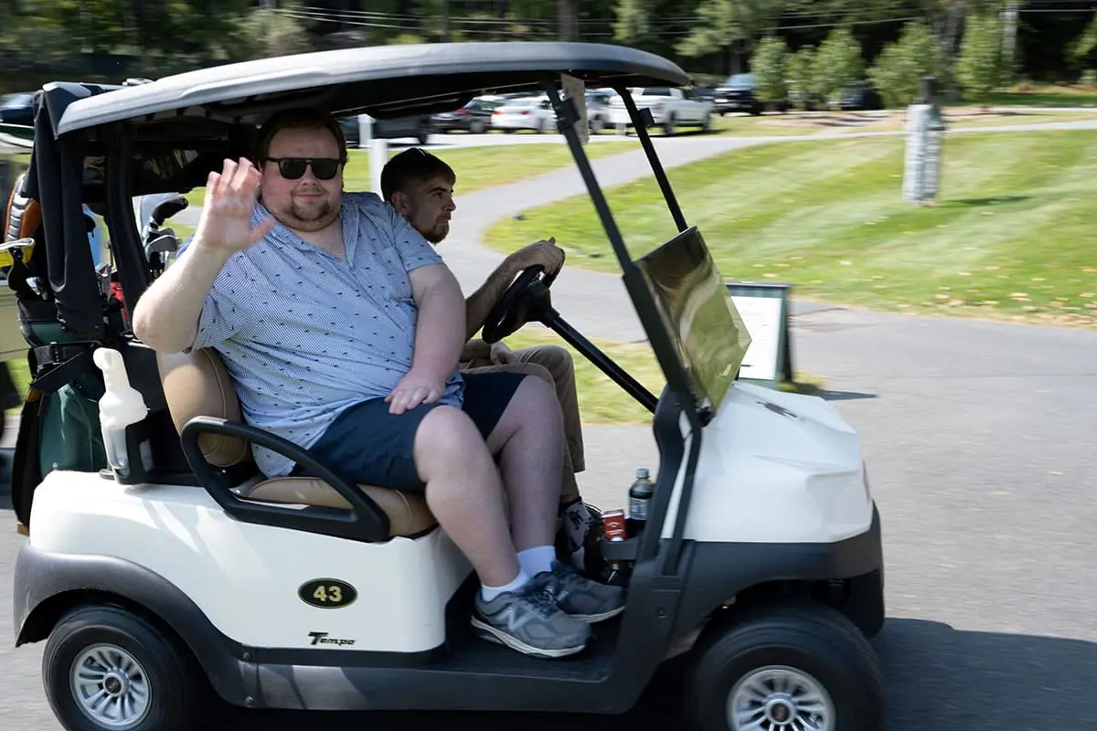A golfer waving from his golf cart